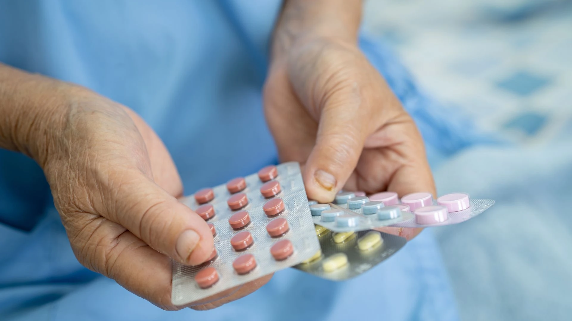 Elderly patient holding various blister packs of medication in their hands.