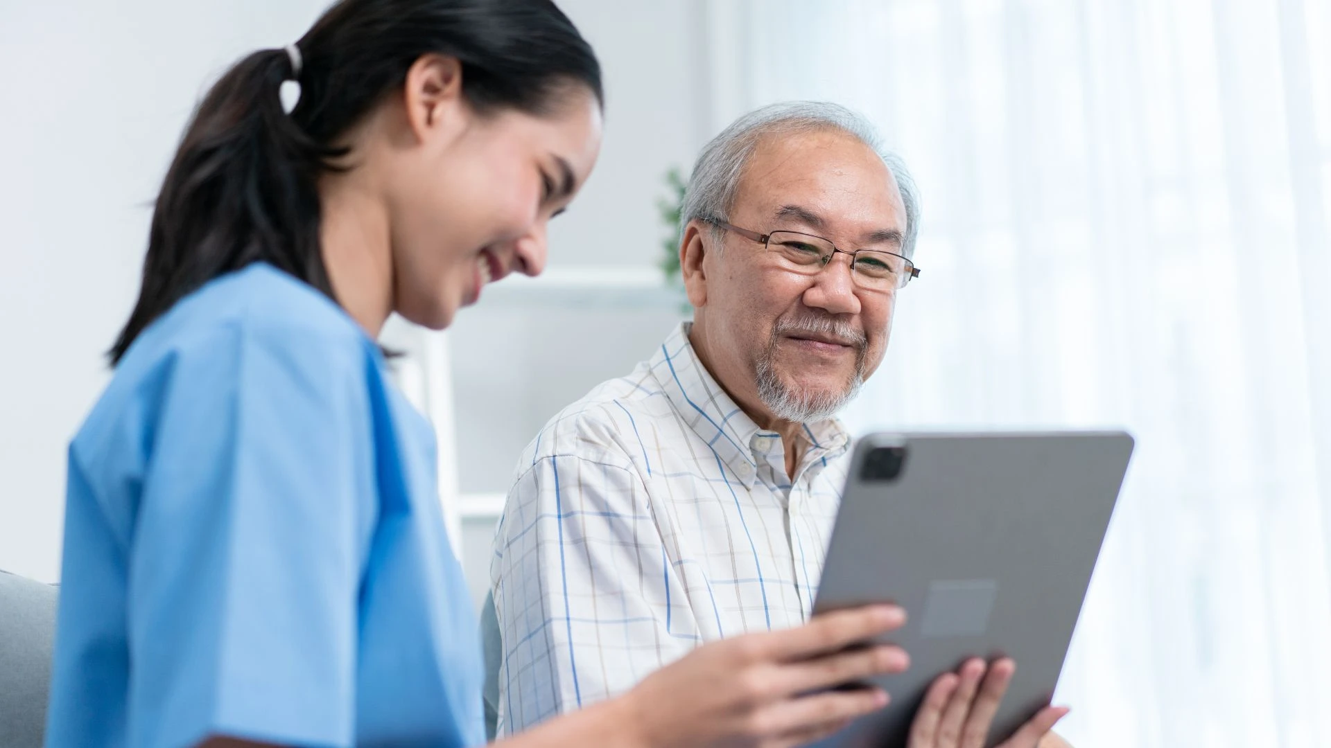 Nurse showing information on a tablet to an elderly male patient during a consultation.